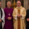 Four Anglican and Catholic clergy members standing together inside a cathedral, wearing traditional religious robes, with a crucifix and stained-glass windows behind them.